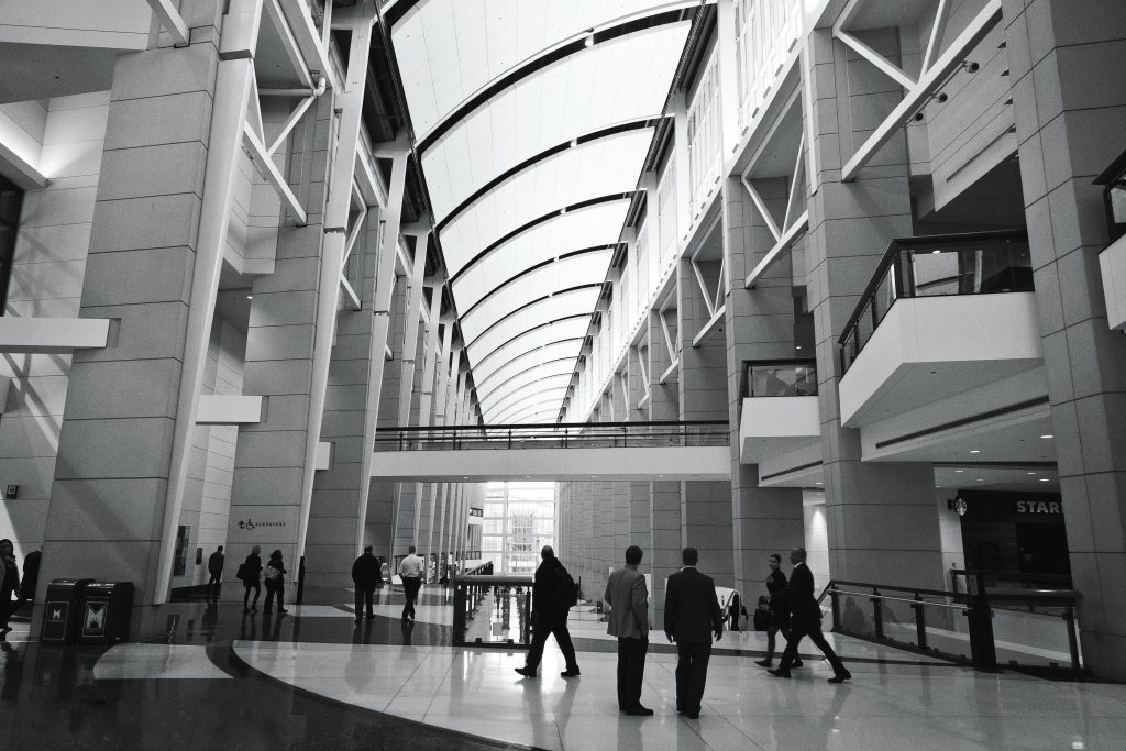 People walking through a large glass-roofed atrium, in black and white